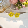 Macro detail of yellow layered flower earrings with golden center on white porcelain tray - Yellow