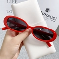 Close-up of red oval cat-eye sunglasses with black lenses on a white leather pouch - Red Frame / Black Grey Lenses