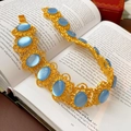 Dettaglio di un bracciale vintage dorato con pietre blu su uno sfondo di un libro - Collana-Blu