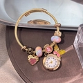 Golden bracelet watch with heart and butterfly charms on a luxury display plate - Gold Butterfly Heart Pink Bangle