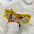 Detail of yellow cat-eye sunglasses with translucent frames held by a hand in white knit - Orange Frame Light Gray Lens