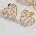 Close-up of heart-shaped gold earring with pearls and zircon on white stone surface - Heart Pearl Earrings