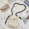 Detailed close-up of a floral canvas crossbody bag with woven strap on a soft white bed - Floral Beige