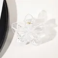 Close-up of flower-shaped transparent acrylic hair claw clip with gold metal spring detail - Clear White