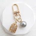 Detailed close-up of golden birdcage pendant with a grey pearl on a polished keychain - Silver Pearl + Birdcage