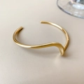 Close-up of a wavy gold-plated open bangle with a polished irregular metallic finish - Gold