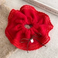 Close-up of a red knitted scrunchie with wave lace edge, bow, and a small metal tag - Red