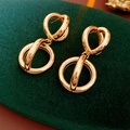 Detailed close-up of golden interlocking circular hoop earrings on green velvet - Gold