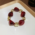 Close-up of red resin and gold metal beads on a white luxury display tray - Bracelet / Red
