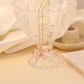 Detailopname van een roze kristallen vlinderhanger aan een gouden ketting op een glas - Roze