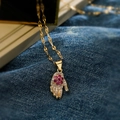 Gold Hamsa Hand necklace with white and pink zircon crystals on blue denim background - Gold with Pink Gemstone