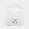 Close-up of white ribbed knit beanie featuring minimalist black sun embroidery detail - White