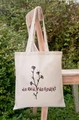 Cream canvas tote bag with No Rain No Flowers floral print hanging on a wooden chair - STD66-B (No Rain No Flowers Floral)