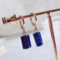 Macro-opname van rechthoekige blauwe lapis lazuli hangers aan gouden oorringetjes - Lapis lazuli