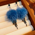 Detailed close-up of blue fur ball earrings with rhinestones and metal tassels in a jewelry box - Stud Earrings / Blue