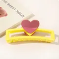 Detailed view of yellow hair claw clip with pink heart on a decorative book background - Heart Hollow Rectangle / Bright Yellow