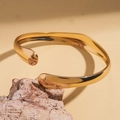Poliertes Goldarmreif in fließendem geometrischem Design auf einem Naturstein-Sockel - Gold