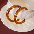 Detail view of amber resin C-shape earrings with marble texture on ceramic cup - Coffee C-Shape