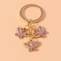 Close-up of golden butterfly keychain with purple enamel wings and sparkling rhinestones - Gold Purple