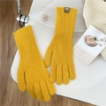 Detail of yellow knitted gloves with brown leather logo tag on a cozy lifestyle setup - One Size / Gold Yellow