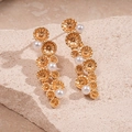 Dettaglio di orecchini a nappa dorati con fiori e perle bianche su sfondo pietra - Oro