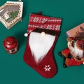 Red knitted Christmas gnome stocking with white beard and snowflake decor on green background - Red