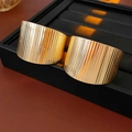 Detail of wide gold-colored rings with vertical pleated texture on black jewelry display tray - Gold (Steel Pin)