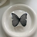 Detailed top view of monochrome butterfly phone grip on a white minimalist ceramic plate - Black and White Realistic Butterfly