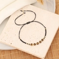 Handgefertigtes Tigerauge-Armband mit schwarzen Perlen und Goldakzenten auf Bambusmatte - Schwarz (Tigerauge)