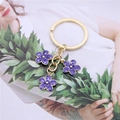 Primer plano de colgantes de flores de esmalte púrpura en llavero dorado elegante - Morado
