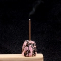 Pink and black floral agate stone incense holder with burning stick and smoke on wood - Rhodonite