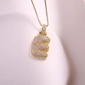 Gros plan d'un collier doré avec pendentif lettre E serti de zircones cubiques pavées - Lettre E