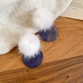 Dettaglio di orecchini a pompon invernali con disco in marmo blu su fondo in legno - Sfera di peluche bianca con disco di marmo blu