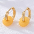 Detail of doughnut-shaped amber stone earrings with gold hoops on white stone background - Amber