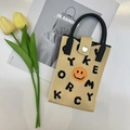 Detail view of beige knit phone bag featuring orange smiley face and black top handle - Smiley Khaki