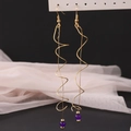 Macro detail of long gold spiral wire earrings with purple bead accent on display - KC Gold (6967)