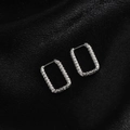 Gros plan de boucles d'oreilles rectangulaires argentées avec texture martelée sur satin - Rectangle Embossé / Acier