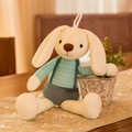 Plush cream bunny toy wearing a teal shirt and grey overalls in a cozy home setting - Light Green