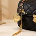 Dettaglio di un medaglione a cuore dorato e nappa su una borsa nera trapuntata - Portachiavi Rotondo d'Oro Stile Cuore