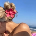 Matte pink flower hair claw clip worn by a model against a beach and blue sky backdrop - Pink