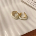 Gold twist hoop earrings with white enamel coating on textured white plate display - Wavy White Hoop Earrings
