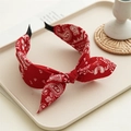Detail of red paisley knotted headband with bow accent on a minimalist beige tray - Red