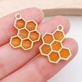 Honeycomb bee charms with orange enamel and gold finish shown on a fingertip - Bee