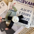 Detail einer schwarzen Satin-Schleifenbrosche mit weißer Kamelie auf einem Vintage-Magazin - Handgefertigte Kamelien-Schleifen-Haarspange