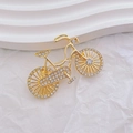 Broche de bicicleta vintage dorado con pedrería sobre fondo blanco ondulado - Dorado