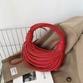 Chic knotted woven handbag in red faux leather placed on a neutral blazer - Red