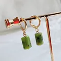Golden hoop earrings featuring cylindrical green natural stone pendants on a T-stand - Xinschan Jade