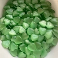 Polished green cat eye stone heart-shaped crystals displayed in a container - Light Green Cat's Eye