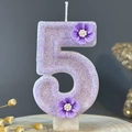 Purple glitter number 5 birthday candle decorated with flowers on a wooden table - Number 5