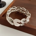 Detalle de pulsera metálica plateada en forma de S con acabado cepillado sobre madera - Plateado